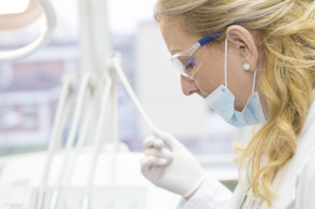 Dental professional in mask, gloves and safety glasses examining an instrument in a bright clinic